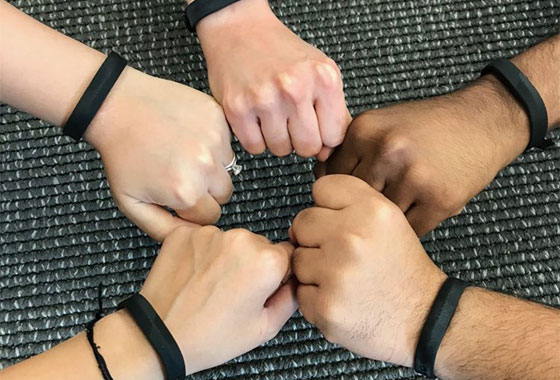 Five hands making fists in a circle. All arms have black Fitbit trackers on them.
