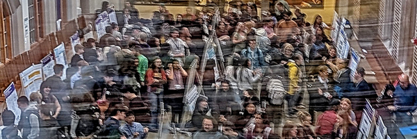 Abstract image of people at a conference looking at posters.
