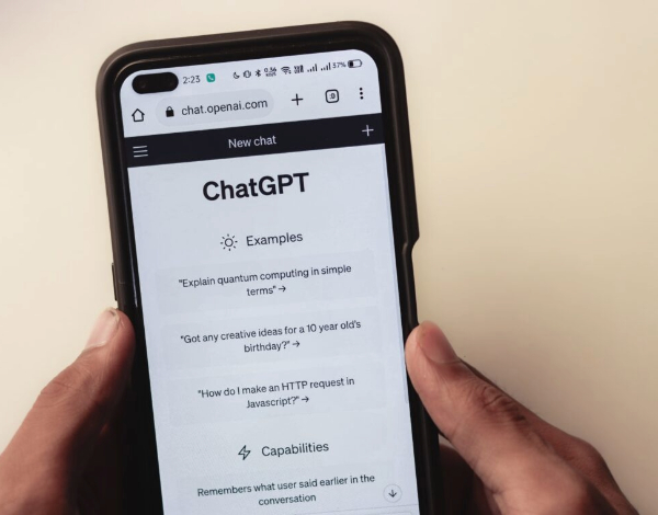 Hands holding a smartphone with ChatGPT on the OpenAI website listed onscreen